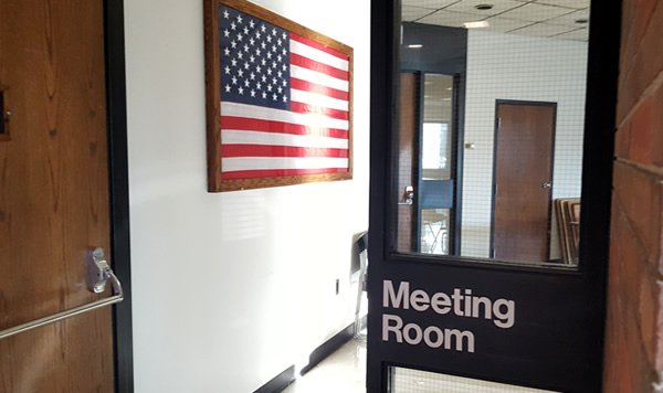 Door and sign for Clinton County Meeting room with an American flag hanging on the wall.